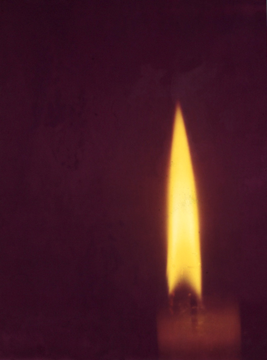 A long yellow candle flame against a dark purple background.