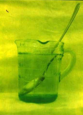 A green-toned still life of a glass jug holding a long brush.